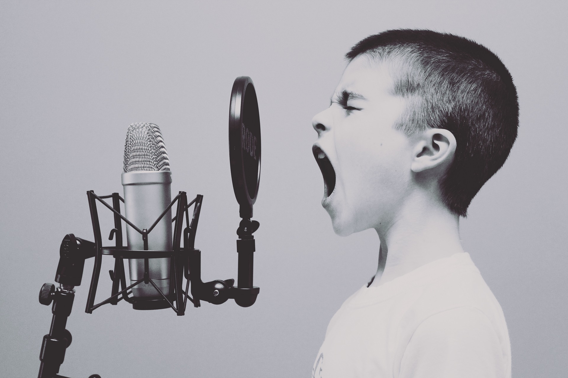 Image is black and white with a boy's profle screaming into a microphone